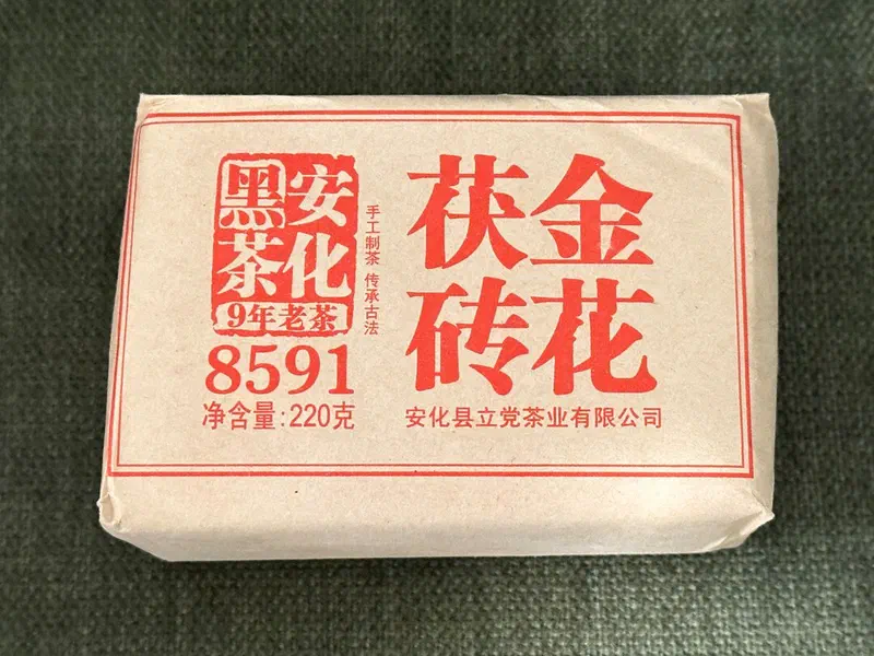 A Fu brick in a kraft paper wrapper printed with red Chinese characters, lying on a green cloth.